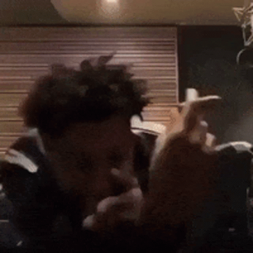 A Man With Curly Hair Is Smoking A Cigarette In Front Of A Wooden Wall . GIF