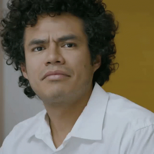 A Man With Curly Hair Is Wearing A White Shirt And Looking At The Camera GIF