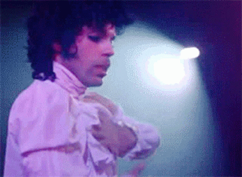 A Man With Curly Hair Is Wearing A White Shirt With Ruffles On The Sleeves GIF