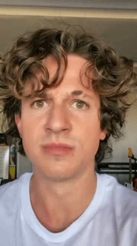 A Man With Curly Hair Is Wearing A White T-Shirt And Making A Funny Face GIF