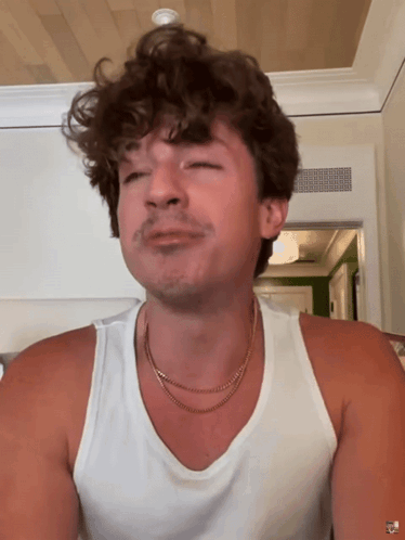 A Man With Curly Hair Is Wearing A White Tank Top And A Gold Necklace GIF