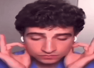 A Man With Curly Hair Is Wearing Headphones And Making A Funny Face With His Hands . GIF