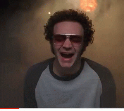 A Man With Curly Hair Wearing Sunglasses And A White Shirt With His Mouth Open GIF