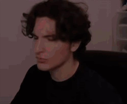 A Man With Dark Hair Is Sitting In A Chair And Making A Funny Face . GIF