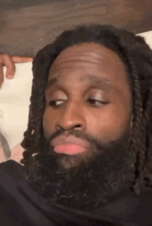 A Man With Dreadlocks And A Beard Is Making A Funny Face While Sitting On A Bed . GIF