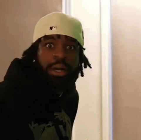 A Man With Dreadlocks And A Beard Wearing A White Hat And A Black Hoodie Is Making A Funny Face . GIF