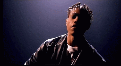 A Man With Dreadlocks And A Black Leather Jacket Looks At The Camera GIF