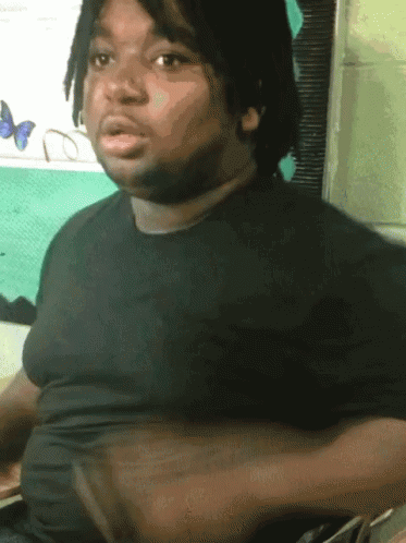 A Man With Dreadlocks And A Black Shirt Is Sitting In Front Of A Window With Butterflies On It GIF