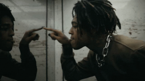 A Man With Dreadlocks And A Chain Around His Neck Looks At Himself In A Mirror GIF