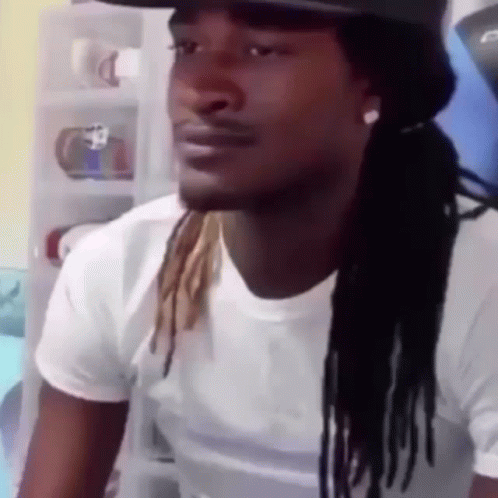 A Man With Dreadlocks And A Hat Is Wearing A White Shirt And A Hat . GIF