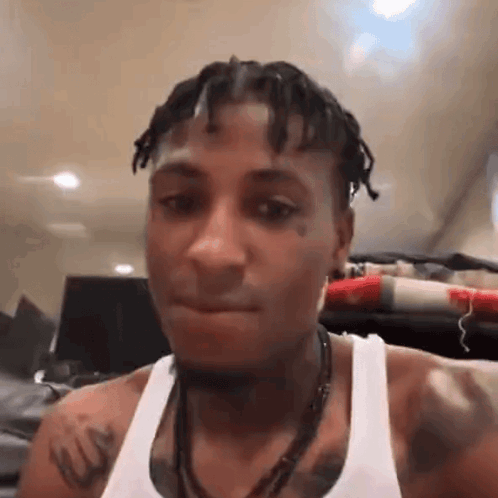 A Man With Dreadlocks And A Tattoo On His Chest Is Wearing A White Tank Top And A Necklace . GIF