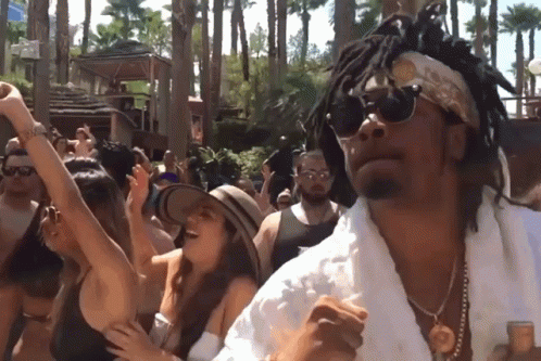 A Man With Dreadlocks And Sunglasses Is Dancing In Front Of A Crowd Of People GIF