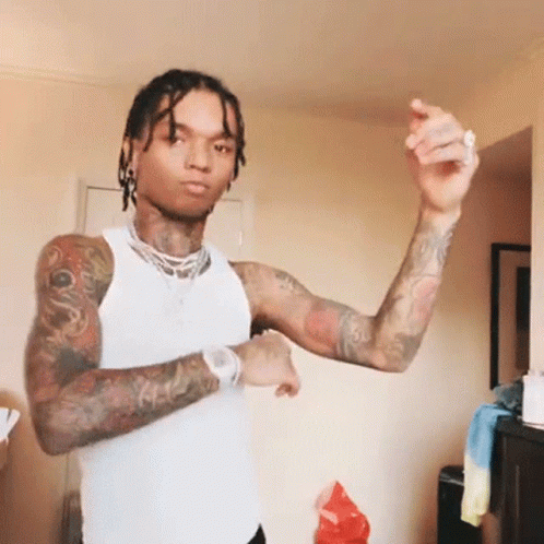 A Man With Dreadlocks And Tattoos Is Wearing A White Tank Top And Dancing . GIF
