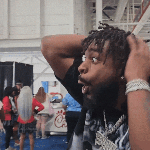 A Man With Dreadlocks Has His Hands On His Head And A Chick-Fil-A Sign In The Background GIF