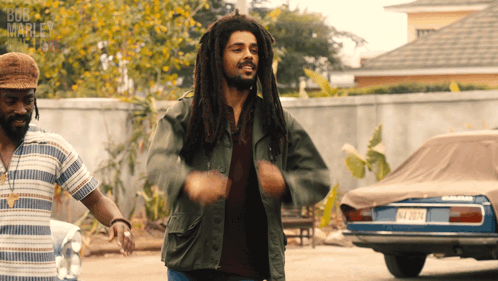 A Man With Dreadlocks Is Dancing In Front Of A Bob Marley Sign GIF