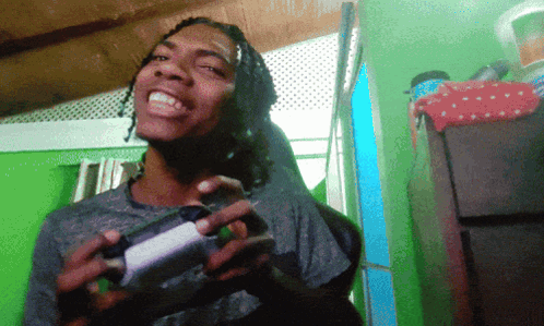 A Man With Dreadlocks Is Holding A Game Controller And Smiling GIF
