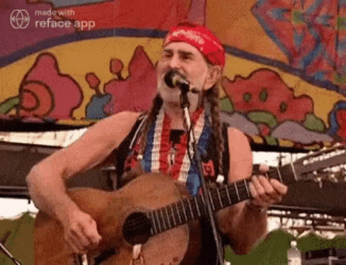 A Man With Dreadlocks Is Playing A Guitar And Singing Into A Microphone . GIF