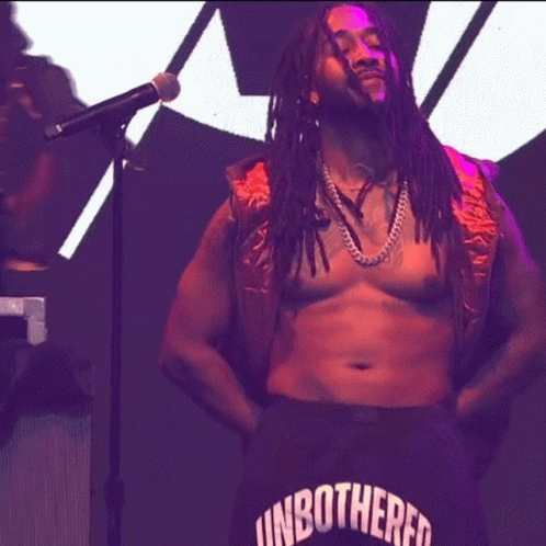 A Man With Dreadlocks Is Singing Into A Microphone While Wearing Shorts That Say Unbothered GIF