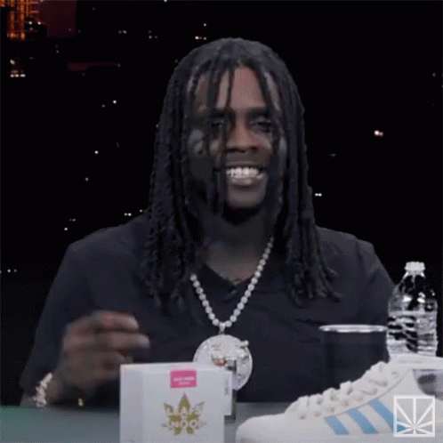 A Man With Dreadlocks Is Sitting At A Table With A Bottle Of Water And A Pair Of Adidas Sneakers GIF
