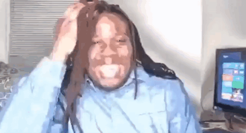 a man with dreadlocks is sitting in front of a computer and holding his hair .
