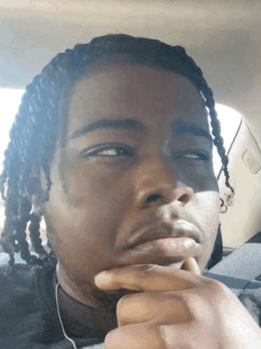 A Man With Dreadlocks Is Sitting In The Back Seat Of A Car With His Hand On His Chin GIF