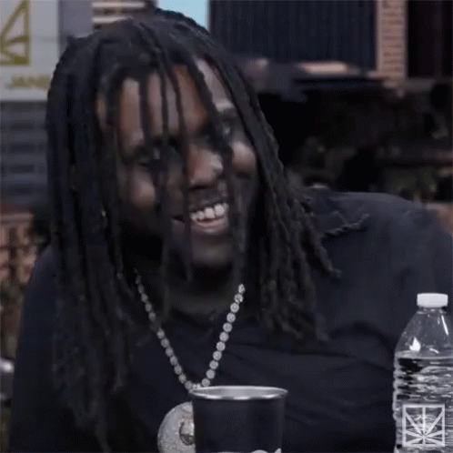 A Man With Dreadlocks Is Smiling While Sitting At A Table With A Bottle Of Water GIF
