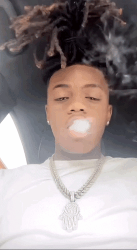 A Man With Dreadlocks Is Smoking A Cigarette In A Car While Wearing A Necklace . GIF