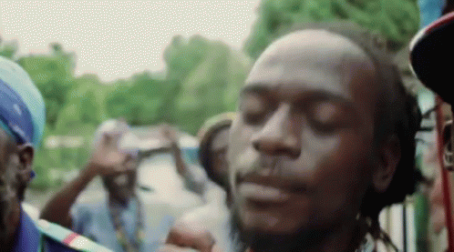 A Man With Dreadlocks Is Smoking A Cigarette In Front Of A Crowd Of People With Their Eyes Closed . GIF