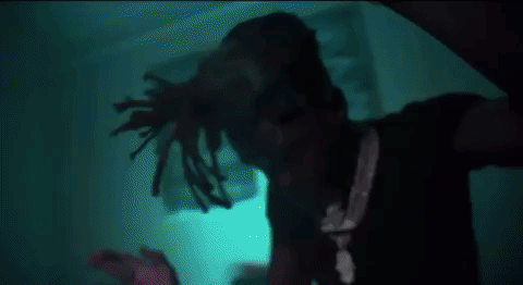 A Man With Dreadlocks Is Standing In A Dark Room In Front Of A Blue Light . GIF