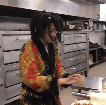 A Man With Dreadlocks Is Standing In A Kitchen In Front Of An Oven . GIF