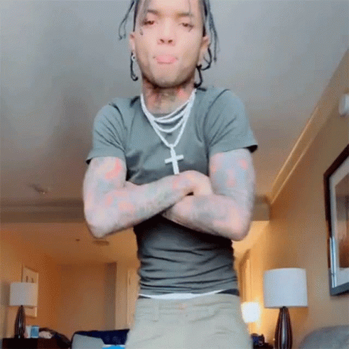 A Man With Dreadlocks Is Standing In A Living Room With His Arms Crossed GIF