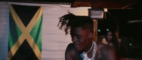 A Man With Dreadlocks Is Standing In Front Of A Flag . GIF