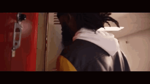 A Man With Dreadlocks Is Standing In Front Of A Red Locker In A Hallway . GIF