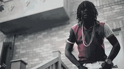 A Man With Dreadlocks Is Standing On A Set Of Stairs In Front Of A Brick Building . GIF