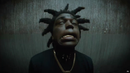 A Man With Dreadlocks Is Wearing A Black Shirt And Gold Chain GIF
