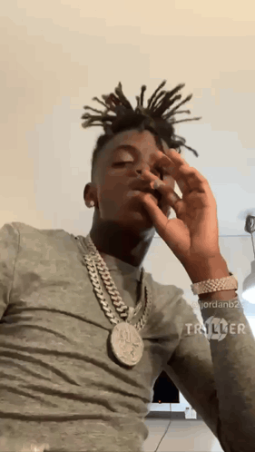 A Man With Dreadlocks Is Wearing A Chain Around His Neck And Smoking A Cigarette GIF