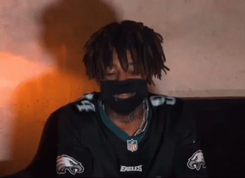 A Man With Dreadlocks Is Wearing A Eagles Jersey And A Mask . GIF