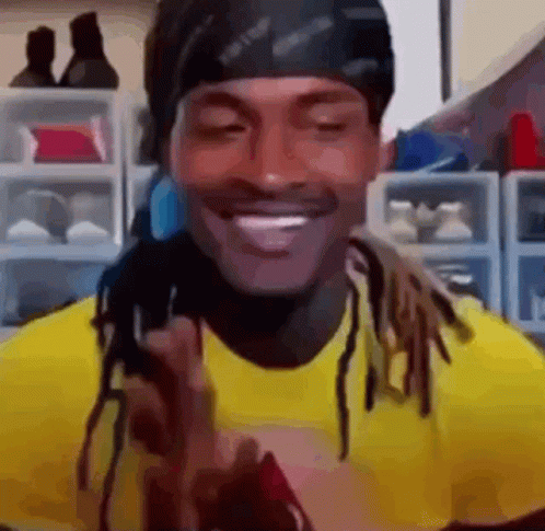 A Man With Dreadlocks Is Wearing A Yellow Shirt And A Black Headband And Smiling . GIF