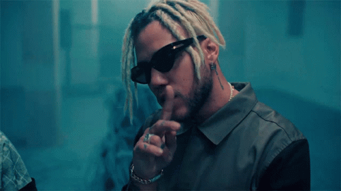 A Man With Dreadlocks Wearing Sunglasses Has His Finger On His Mouth GIF