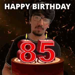 A Man With Glasses And A Beard Is Holding A Birthday Cake With Candles In The Shape Of The Number 85 GIF