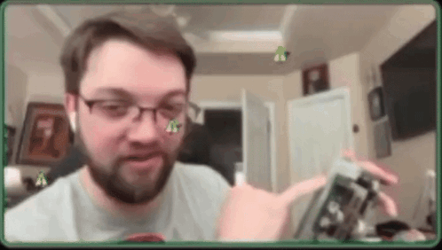 A Man With Glasses And A Beard Is Holding A Cell Phone In A Room . GIF