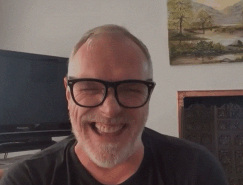 A Man With Glasses And A Beard Is Laughing In Front Of A Panasonic Television GIF