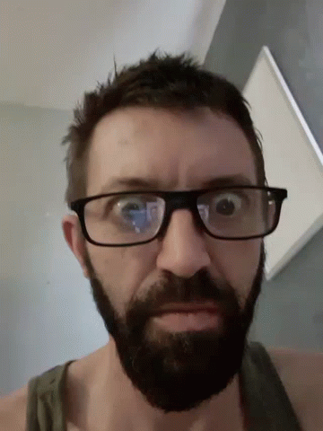 A Man With Glasses And A Beard Is Looking Down GIF