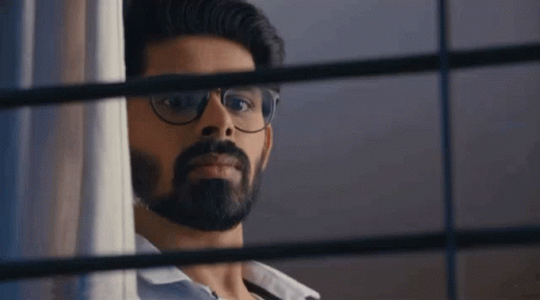 A Man With Glasses And A Beard Is Peeking Out Of A Window . GIF