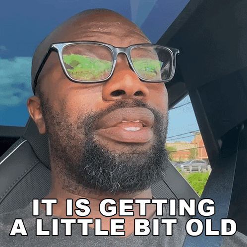 A Man With Glasses And A Beard Is Sitting In A Car With The Words It Is Getting A Little Bit Old Below Him GIF