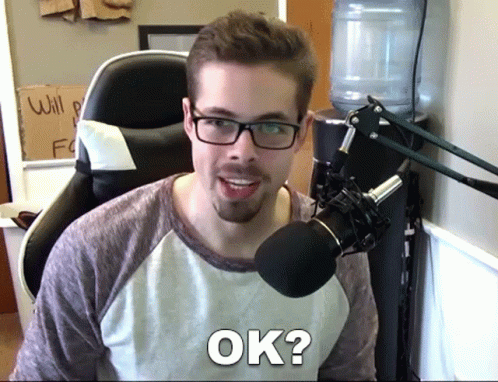 a man with glasses and a beard is sitting in front of a microphone and saying ok
