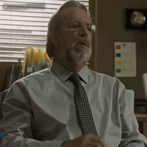 A Man With Glasses And A Beard Is Sitting In Front Of A Window With A Sign That Says #Diggstown On It GIF