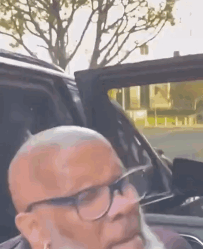 A Man With Glasses And A Beard Is Sitting In The Back Seat Of A Car . GIF