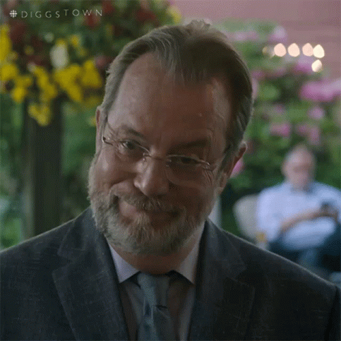 A Man With Glasses And A Beard Is Smiling And Looking At The Camera . GIF