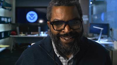 A Man With Glasses And A Beard Is Smiling In Front Of A Screen That Says U.s. Navy GIF